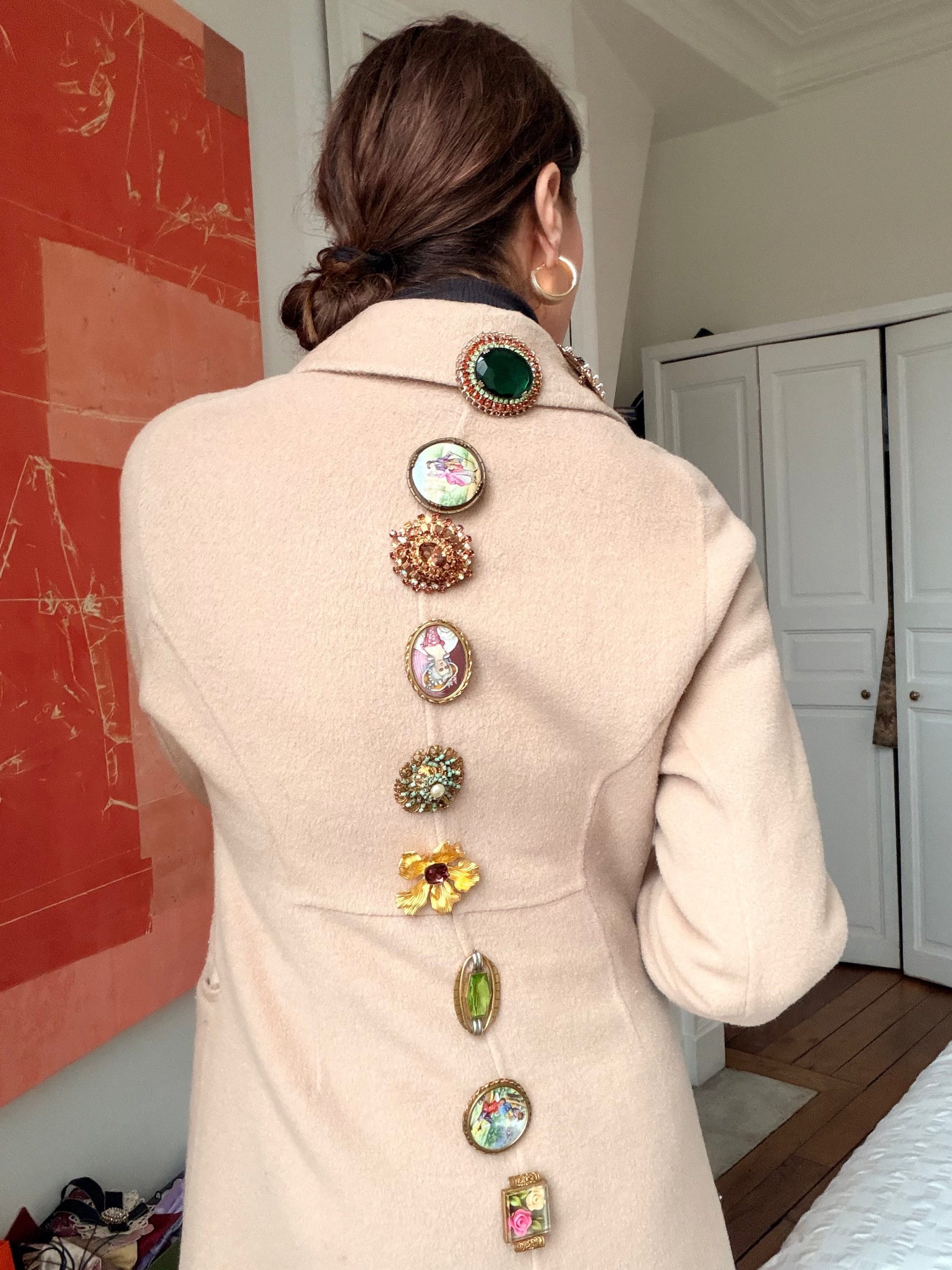 Artful Back Detail: A Line of Diverse Brooches on a Beige Wool Coat Artful Back Detail: A Line of Diverse Brooches on a Beige Wool Coat — Brooch Outfits 2027